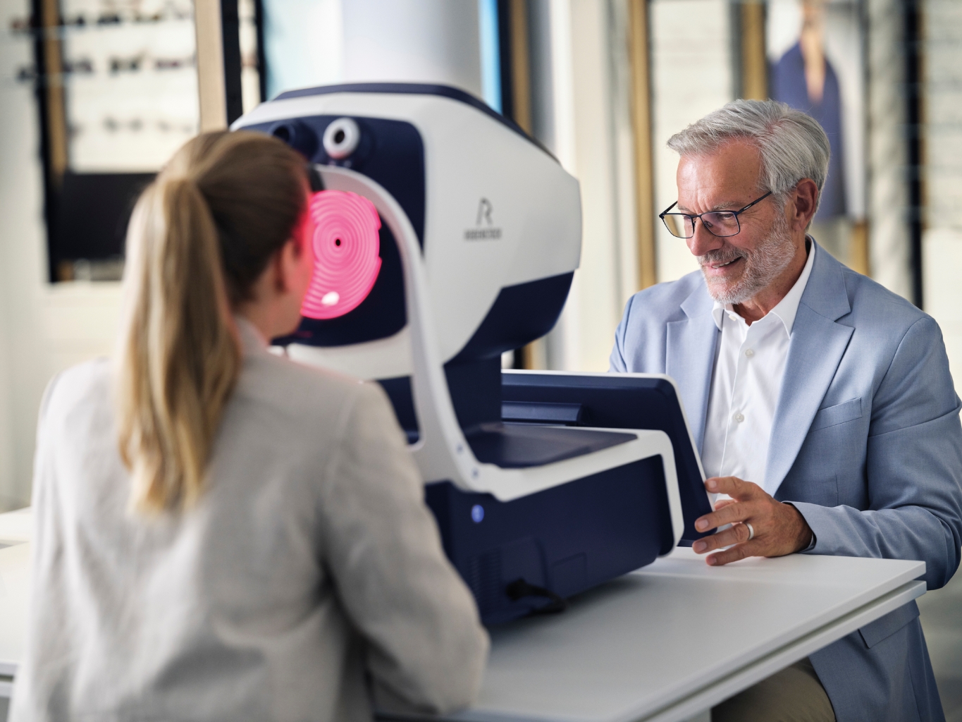 Deux personnes dans un magasin d’optique utilisent un appareil de mesure biométrique Rodenstock avec écran tactile pour l’ajustement précis des verres. 