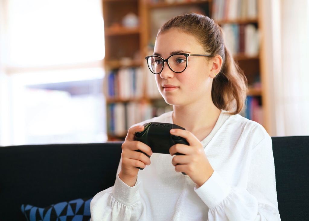 Mädchen sitzt auf einem Sofa und hält einen Spielecontroller in der Hand 