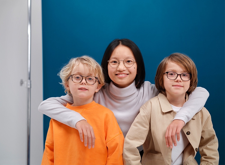 zwei Jungen und ein Mädchen mit Brille schauen gemeinsam in die Kamera 