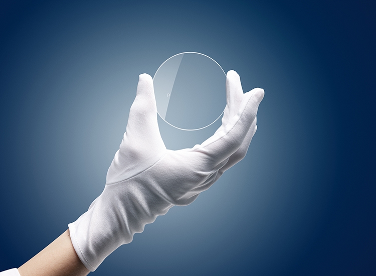 Eine Hand mit Handschuh hält ein Brillenglas 