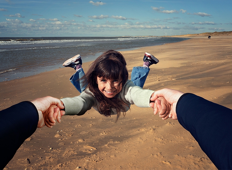 Ein Mädchen wird von einem Elternteil am Strand herumgewirbelt 
